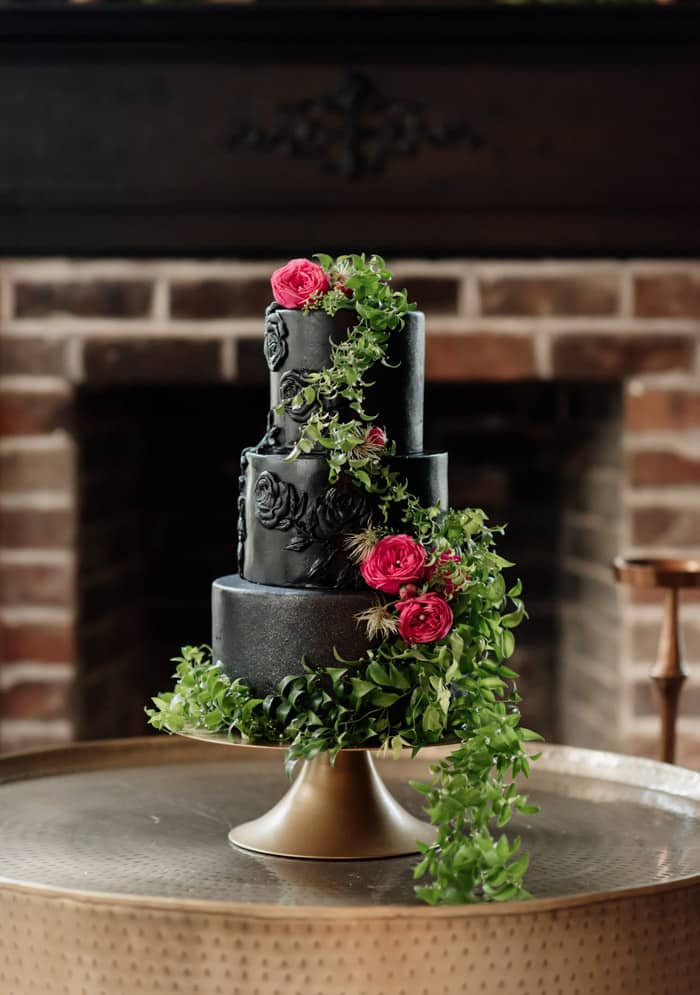 Three tier black wedding cake with dramatic details like greenery and red roses