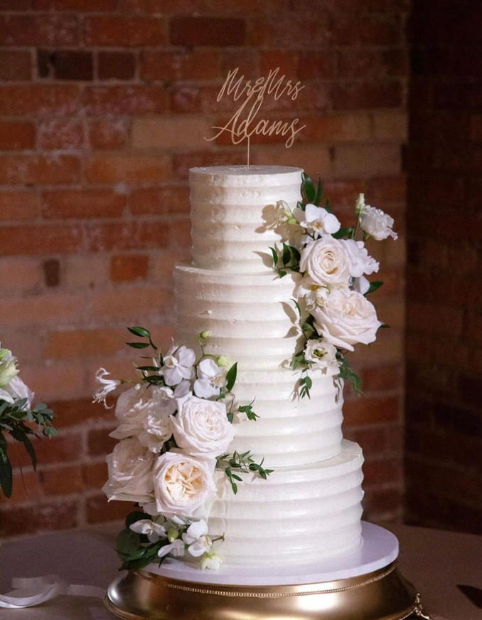 4 tier all white wedding cake with white flowers and greenery